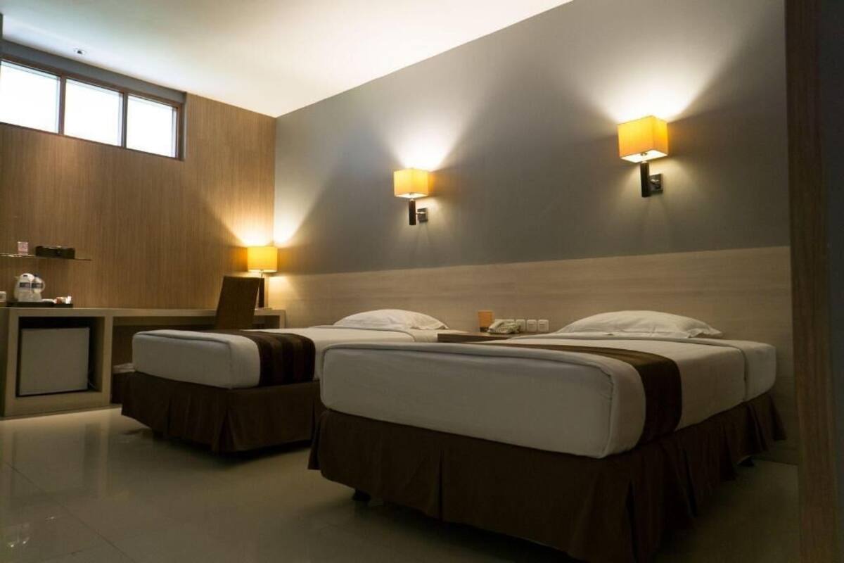 Ein Hotelzimmer mit zwei Betten, einem Schreibtisch, einem Stuhl und zwei Wandleuchten.