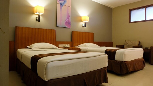 A hotel room with two beds, wooden headboards, bedside lamps, a large abstract painting, and a window. - Hotel Asri Plaza Asia Tasikmalaya (Tasikmalaya)