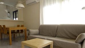 Ein Wohnzimmer mit einem beigefarbenen Sofa, einem Holztisch und einem Essbereich mit Tisch und Stühlen.