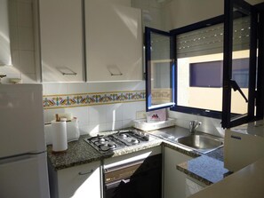 A compact kitchen with a gas stove, sink, and a refrigerator. A window with a view of the outside is visible.