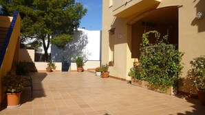 Une cour avec un sol carrelé, des plantes en pot et un bâtiment doté d’un balcon.
