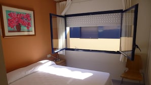 Une chambre à coucher avec un lit, une chaise, une fenêtre avec des rideaux et un tableau accroché au mur.