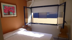 Una camera da letto con un letto, una sedia, una finestra con tende e un quadro appeso al muro.