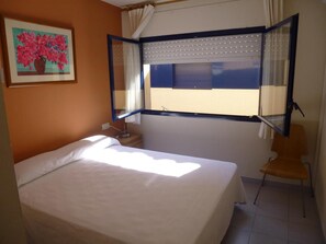 A bedroom with a bed, a chair, a window with curtains, and a painting on the wall.