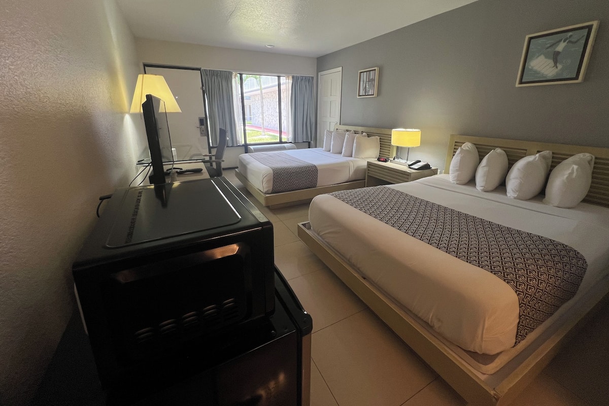 A hotel room with two beds, a desk, a TV, and a window with curtains.