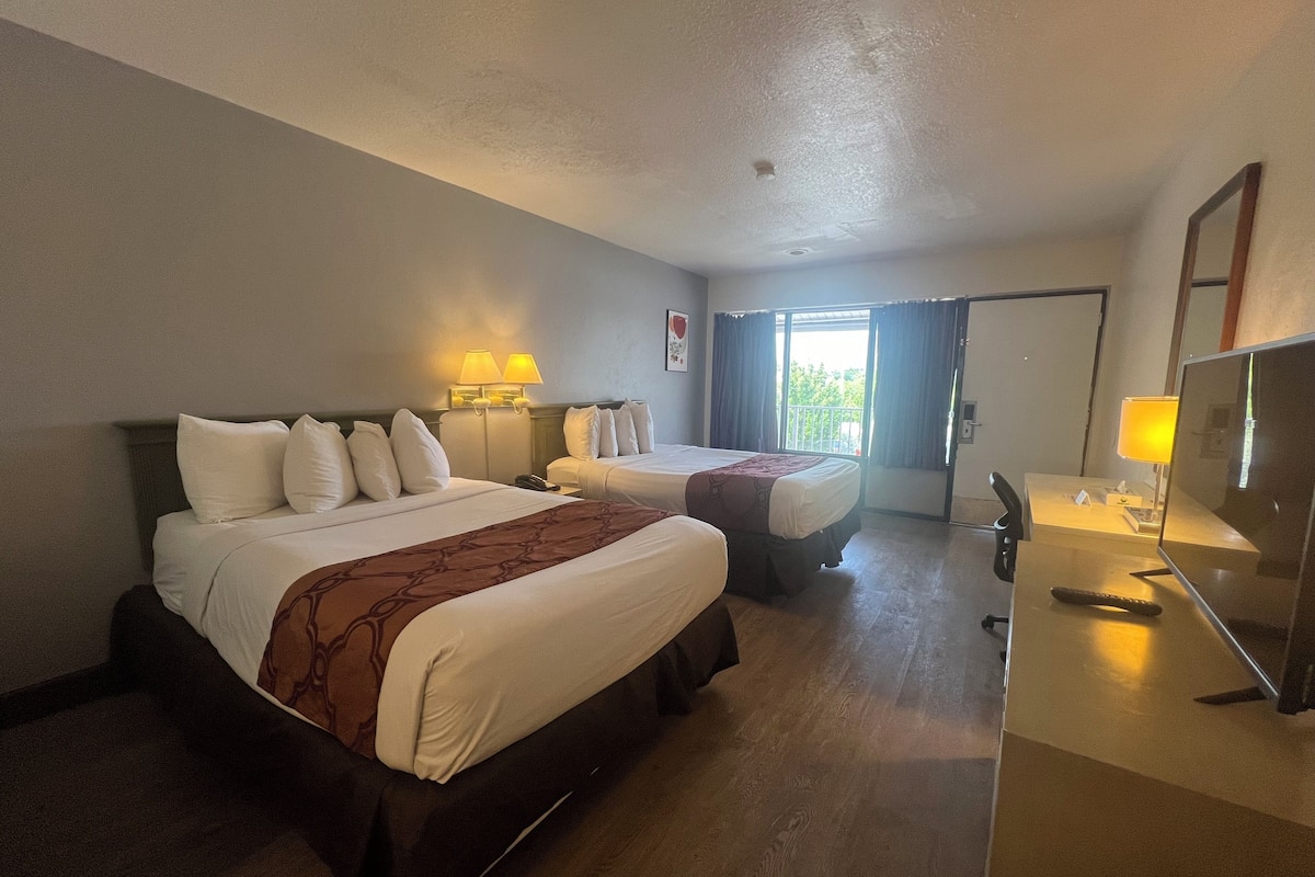 A hotel room with two beds, a desk with a computer, a chair, and a window with curtains.