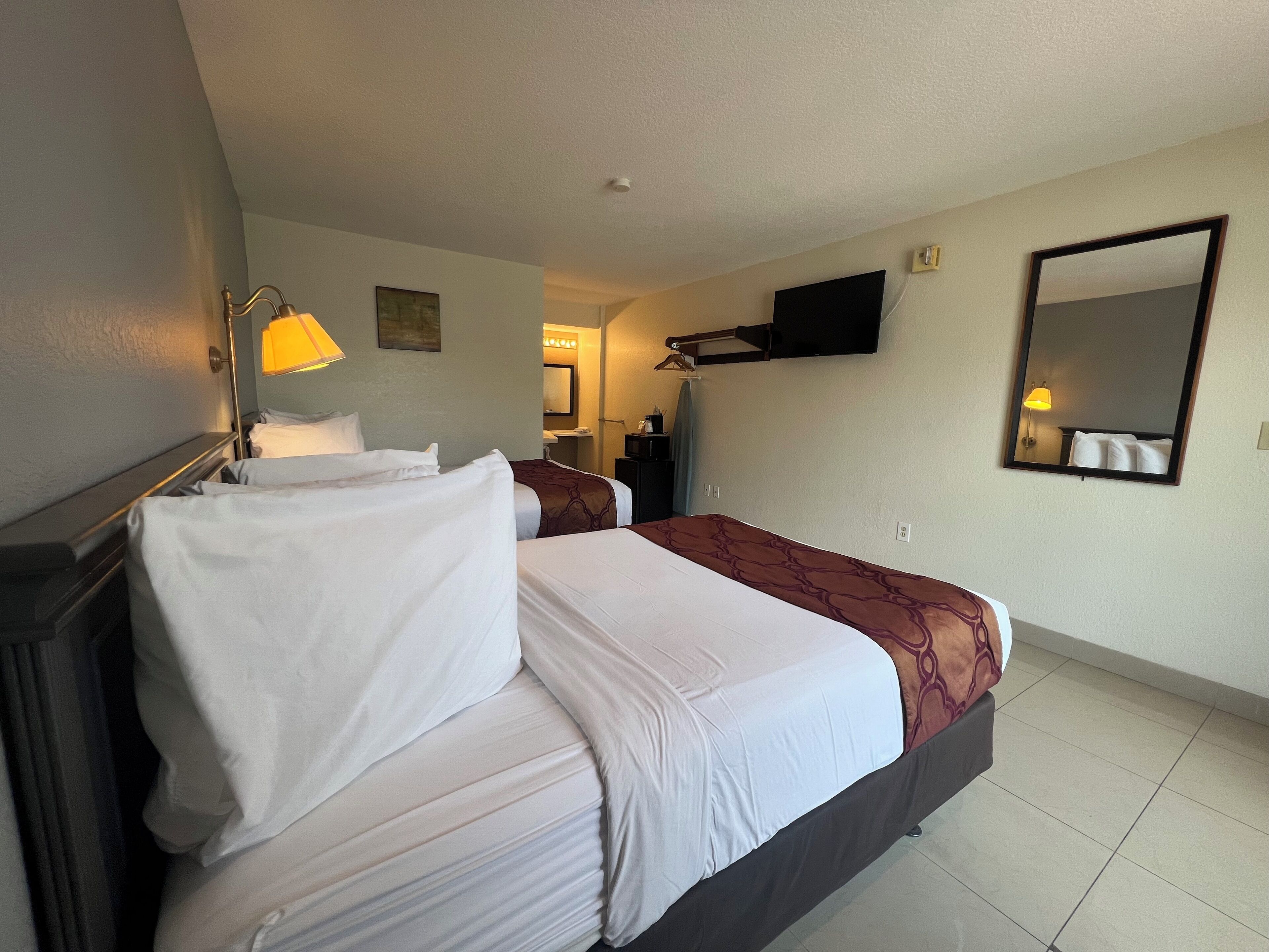 Une chambre d’hôtel avec deux lits, une télévision, un miroir et une lampe.