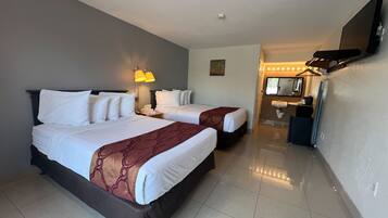 A hotel room with two beds, a bathroom with a sink and mirror, and a small kitchenette.