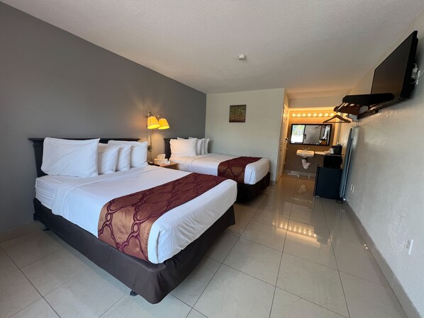 A hotel room with two beds, a bathroom with a sink and mirror, and a small kitchenette.