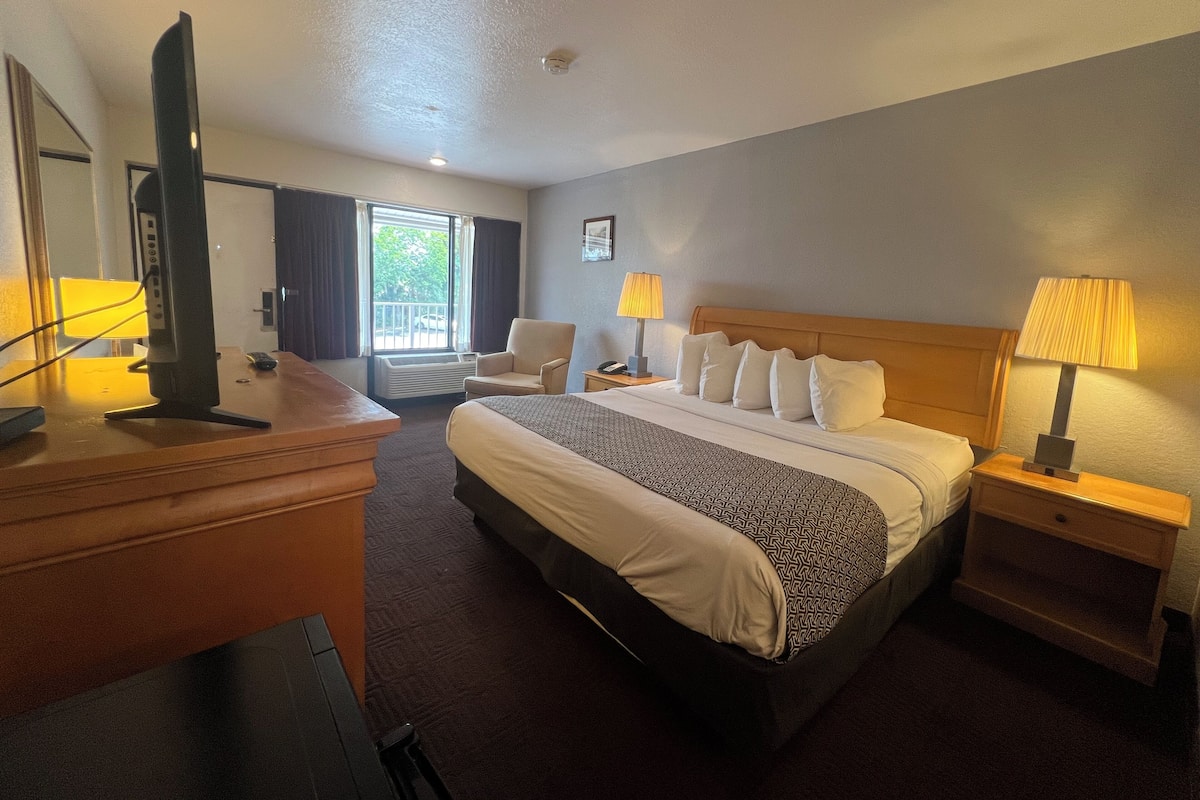 A hotel room with a bed, a desk, a chair, a television, and a window with curtains.