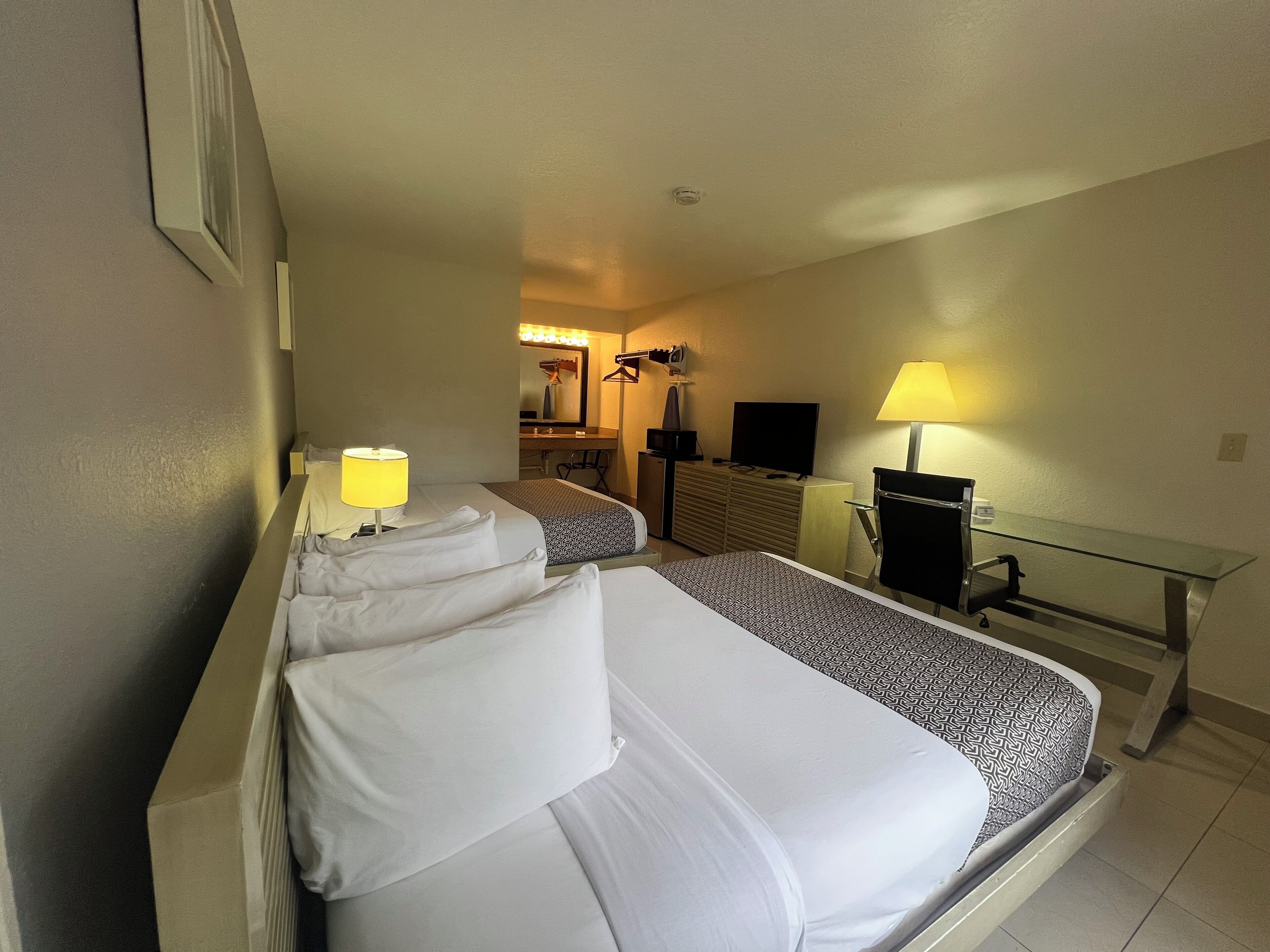 Habitación de hotel con dos camas, un escritorio, una silla, un televisor y un espejo.