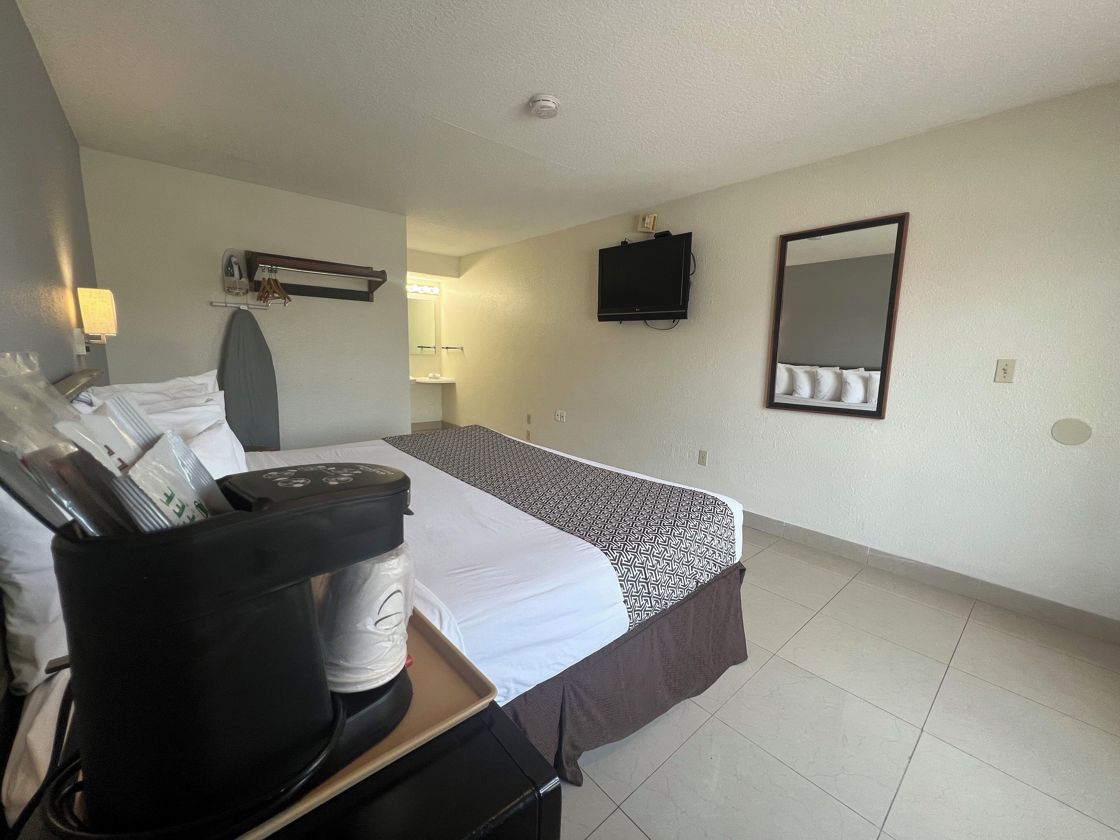 A hotel room with a bed, a TV, a mirror, and a desk with a coffee maker.
