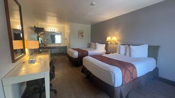 A hotel room with two beds, a desk with a chair, a mirror, and a bathroom visible through an open door.