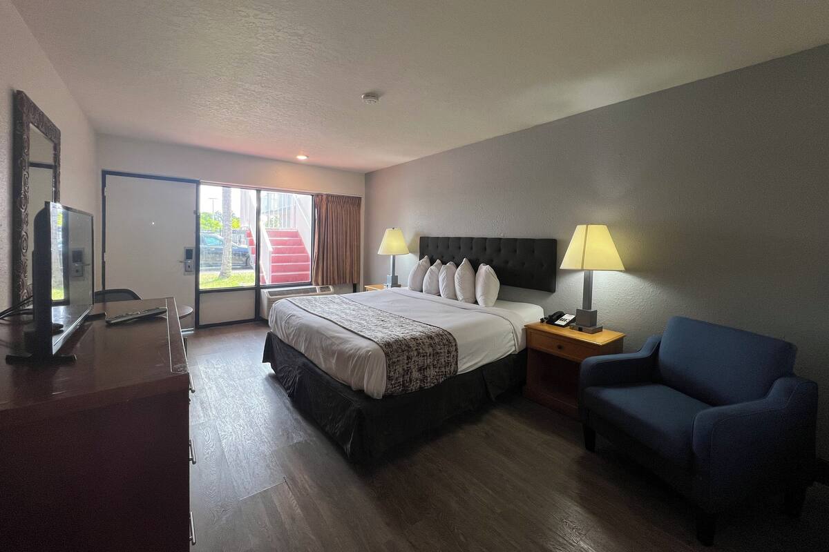 A hotel room with a bed, bedside lamps, a desk with a television, and a chair.