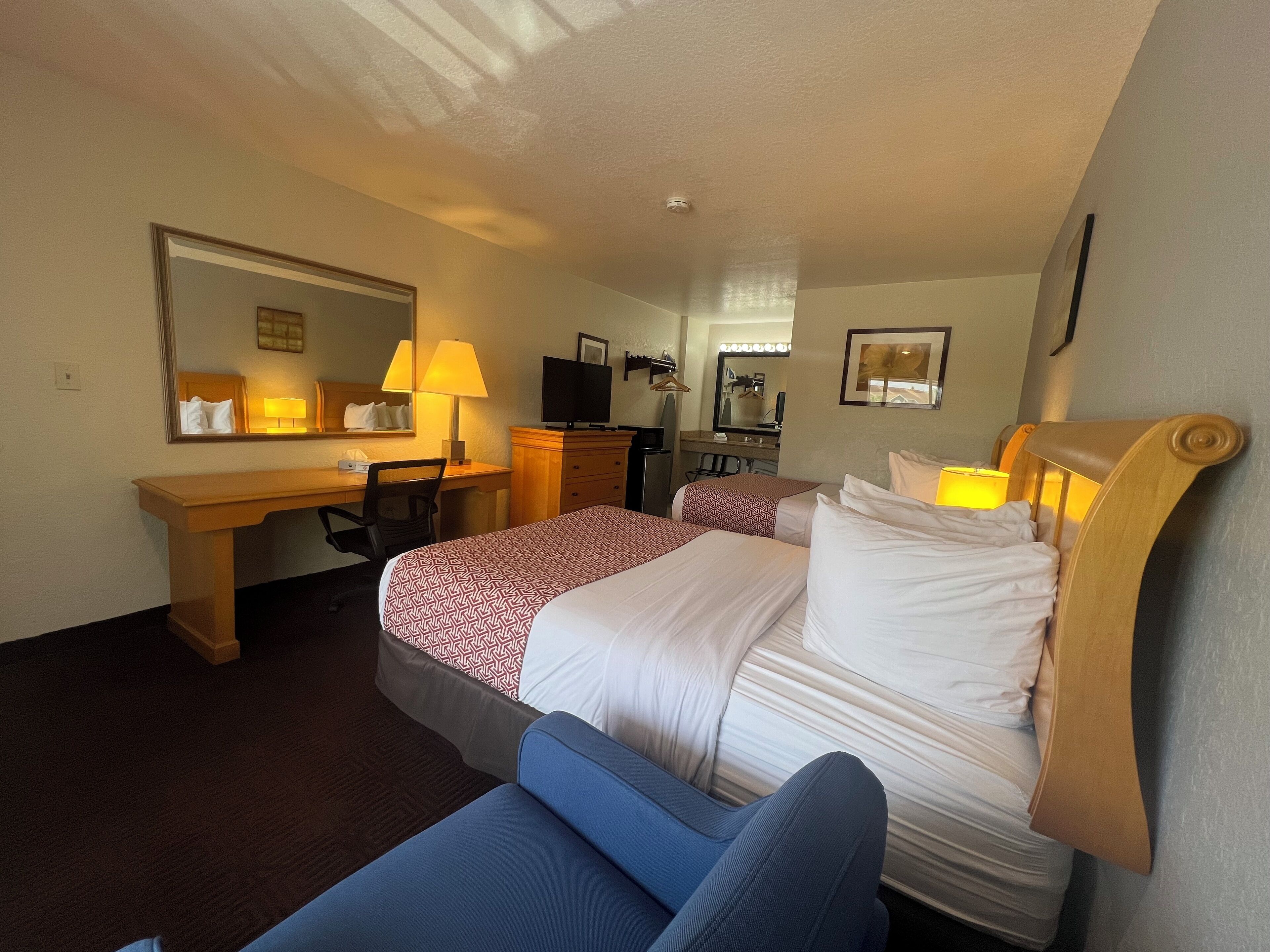 A hotel room with two beds, a desk, a chair, a TV, and a mirror.