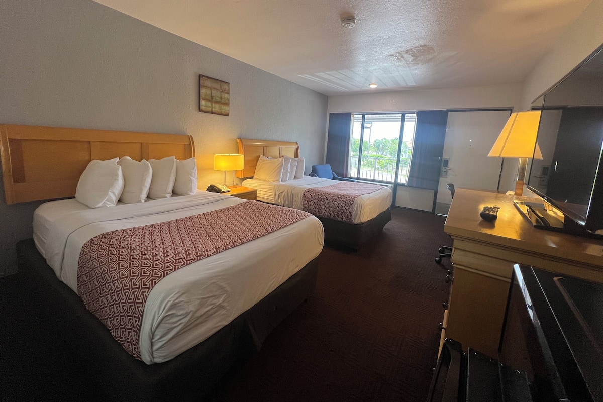 A hotel room with two beds, a desk with a TV, and a window with curtains.