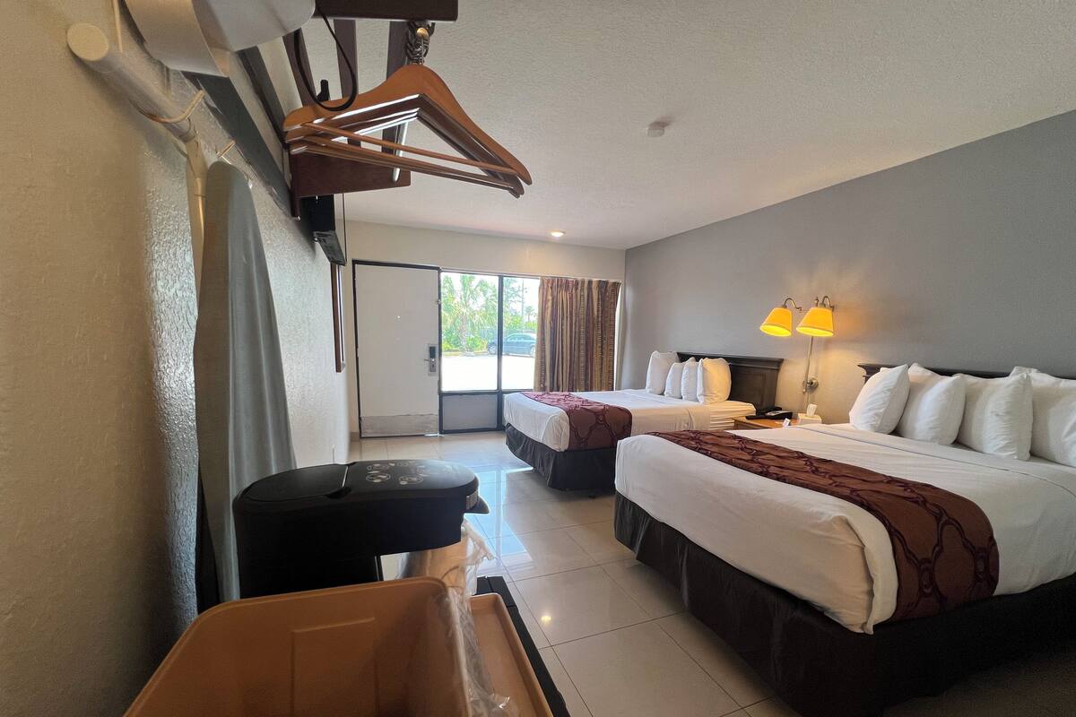 A hotel room with two beds, a desk, a chair, and a trash bin.