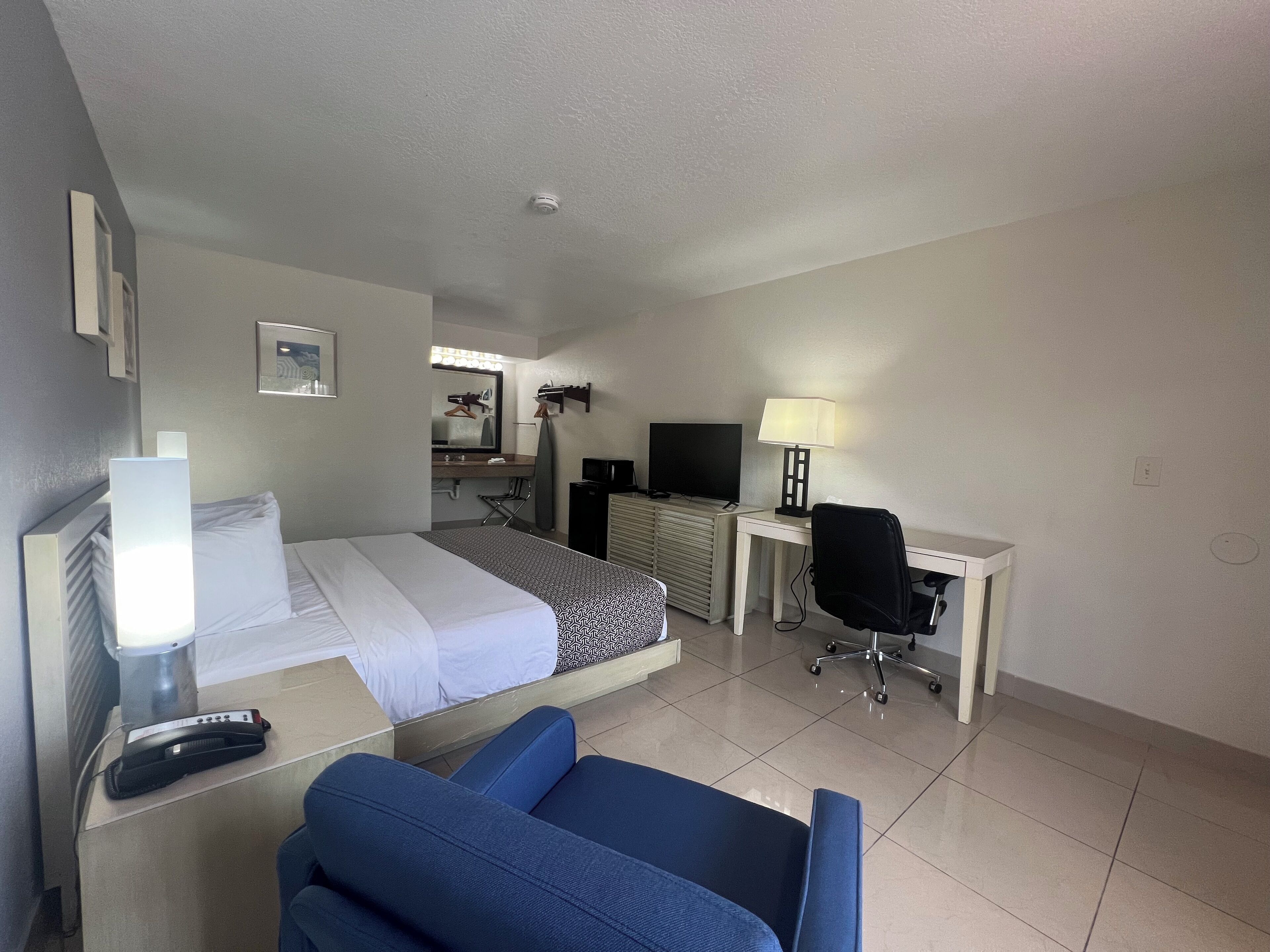 A hotel room with a bed, a desk, a chair, a TV, a lamp, and a mirror.
