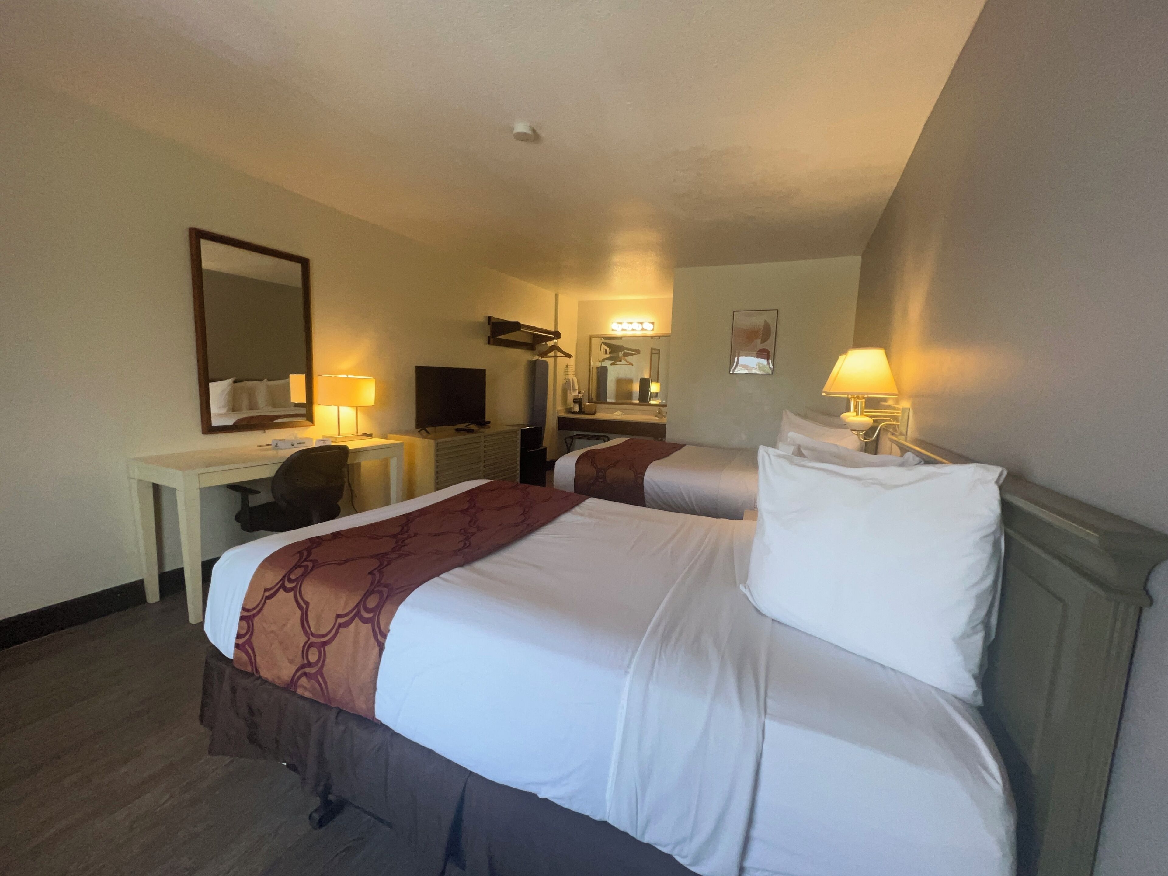 A hotel room with two beds, a desk, a chair, a television, and a mirror.