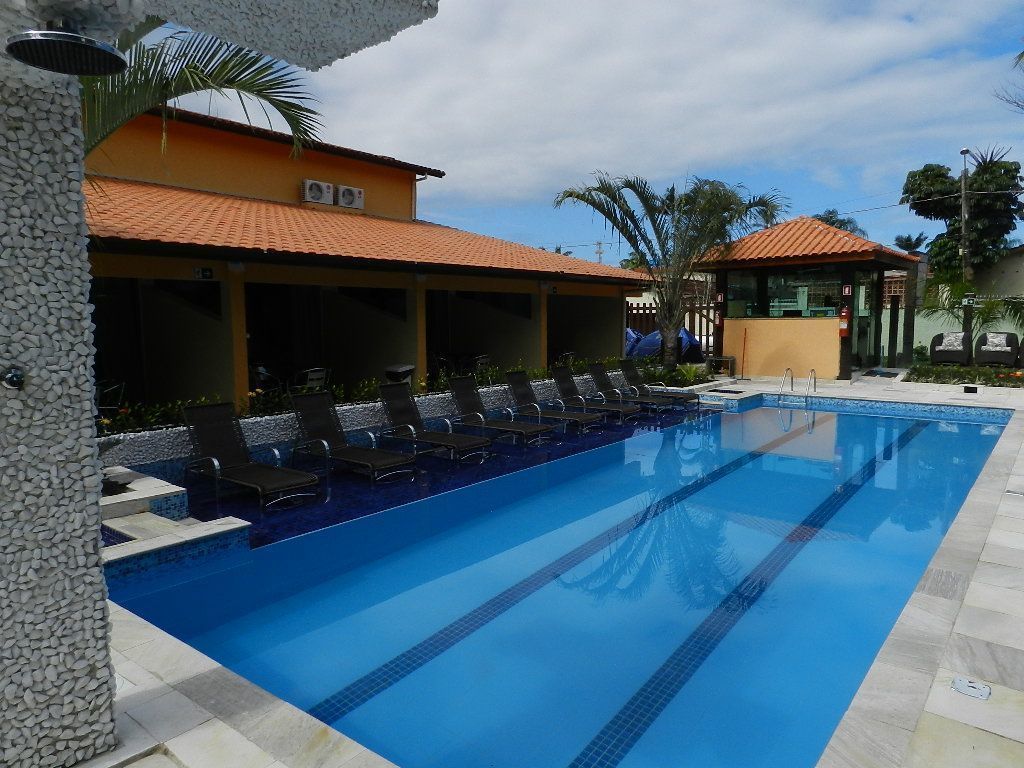A swimming pool with lounge chairs, a covered seating area, and a building with a tiled roof.