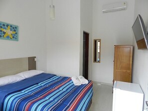 A hotel room with a bed, a television, a wardrobe, and a door. - Pousada Acqua Infinity (Bertioga)