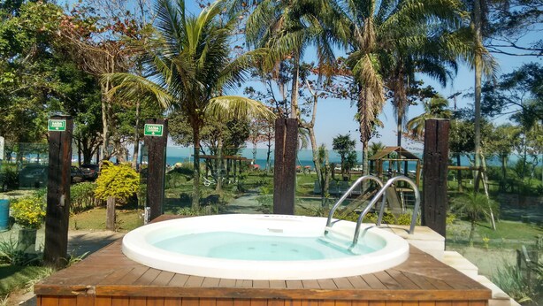 An outdoor hot tub surrounded by tropical vegetation and a view of the sea. - Pousada Acqua Infinity (Bertioga)