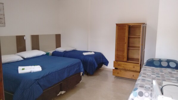 A room with two beds, each with blue bedding and white pillows, a wooden wardrobe, and a small table with a chair. - Pousada Acqua Infinity (Bertioga)