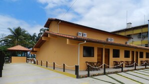 A building with a yellow facade, air conditioning units, and a paved area with yellow lines. - Pousada Acqua Infinity (Bertioga)