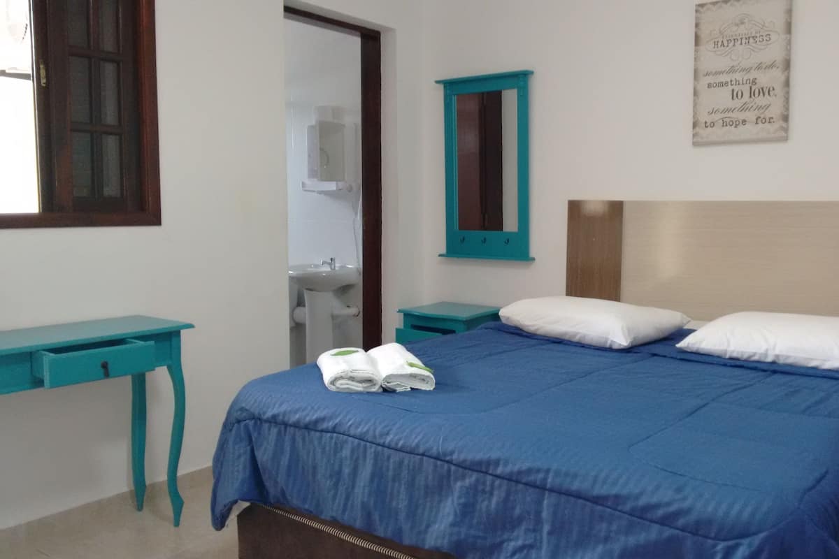 A bedroom with a bed, a nightstand, a desk, a mirror, and a wall with a motivational quote.