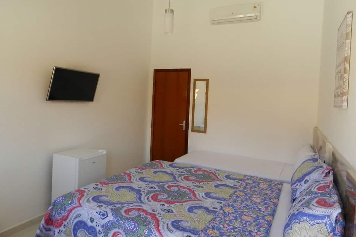 A bedroom with a bed, a television mounted on the wall, a door, and an air conditioning unit.
