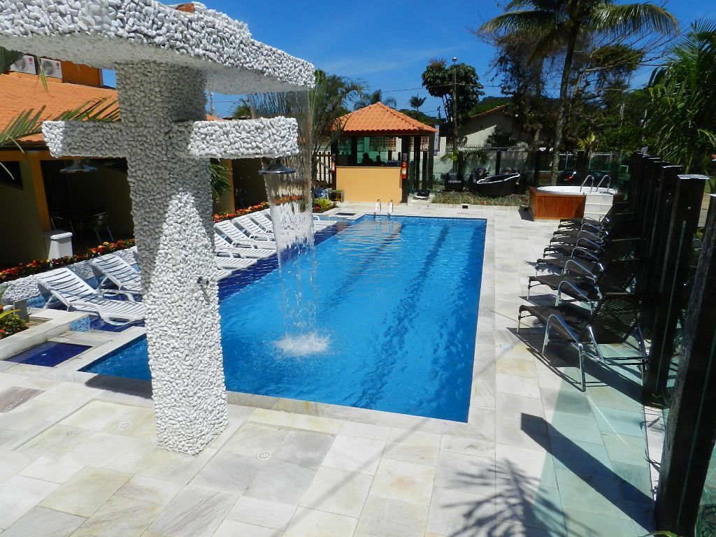 Una piscina con sillones de descanso, un pilar de piedra y un edificio pequeño al fondo.