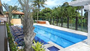 A swimming pool with a clear blue water, surrounded by palm trees and a wooden deck. - Pousada Acqua Infinity (Bertioga)