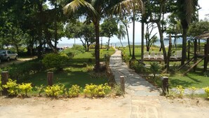 A paved pathway leading to a beach area with chairs and a small wooden structure. - Pousada Acqua Infinity (Bertioga)