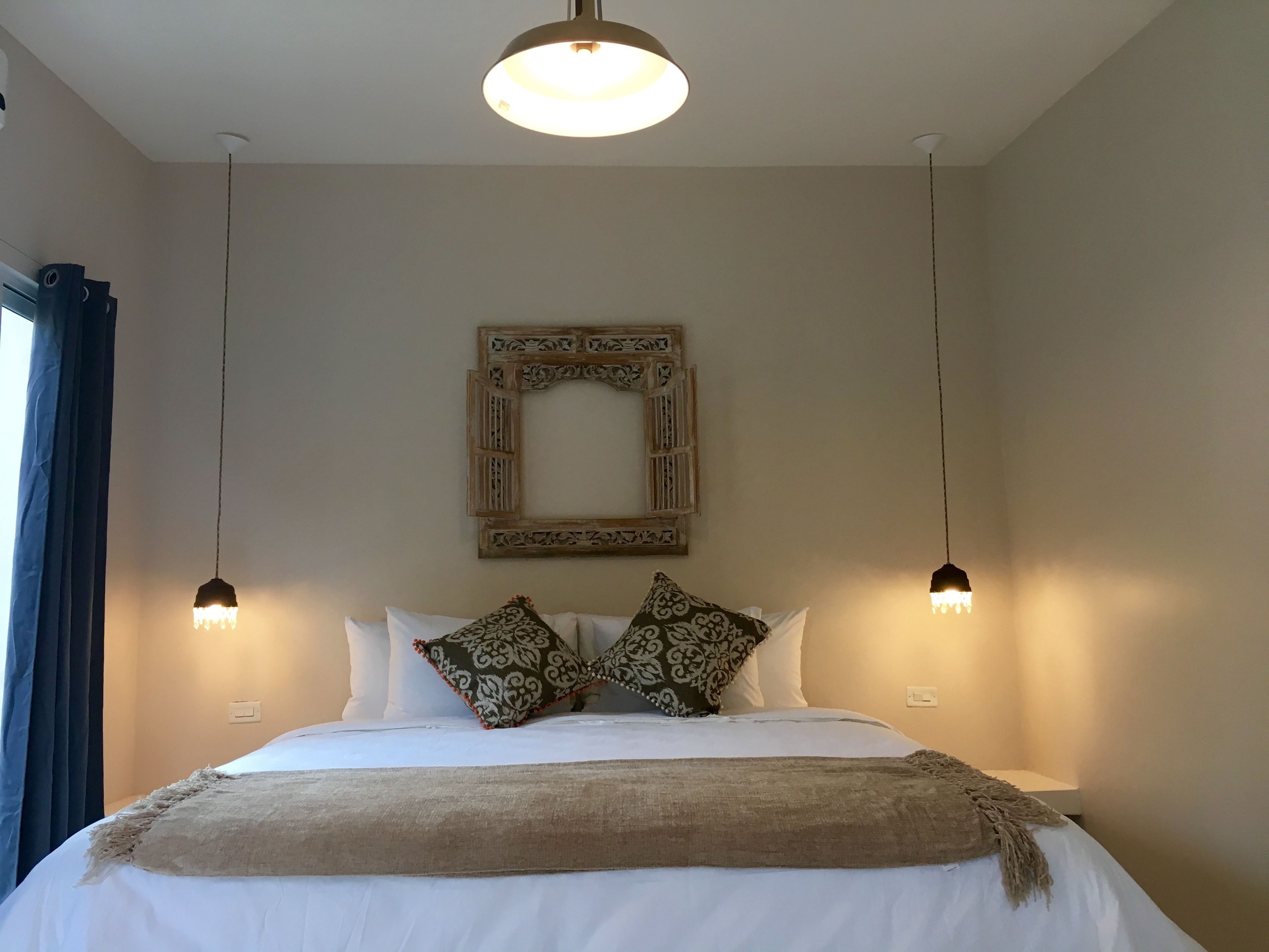 Una cama bien hecha con un edredón estampado, dos almohadas decorativas y una lámpara colgante arriba.