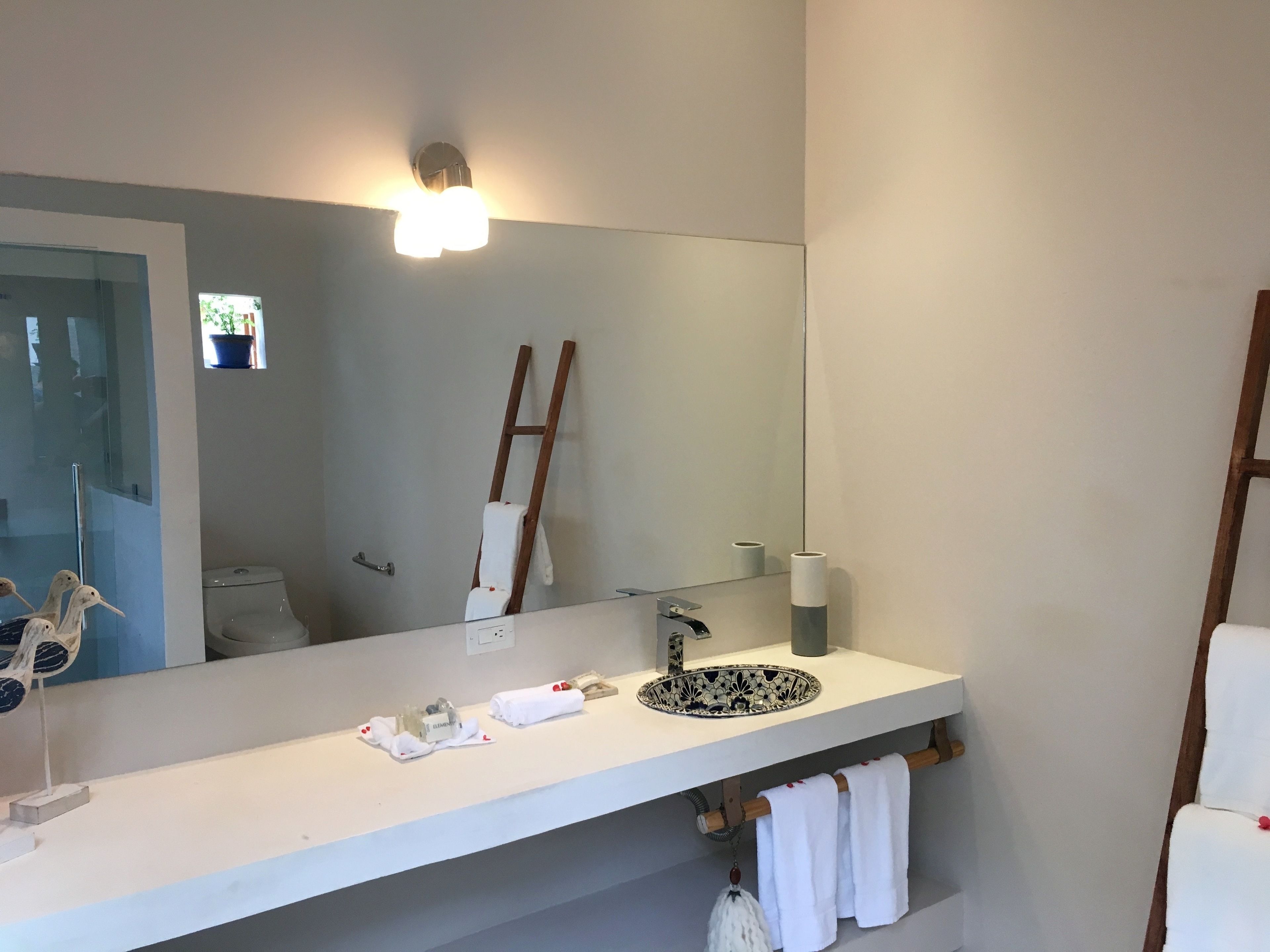 A modern bathroom with a white vanity, a large mirror, a sink with a decorative basin, and a towel rack with towels.