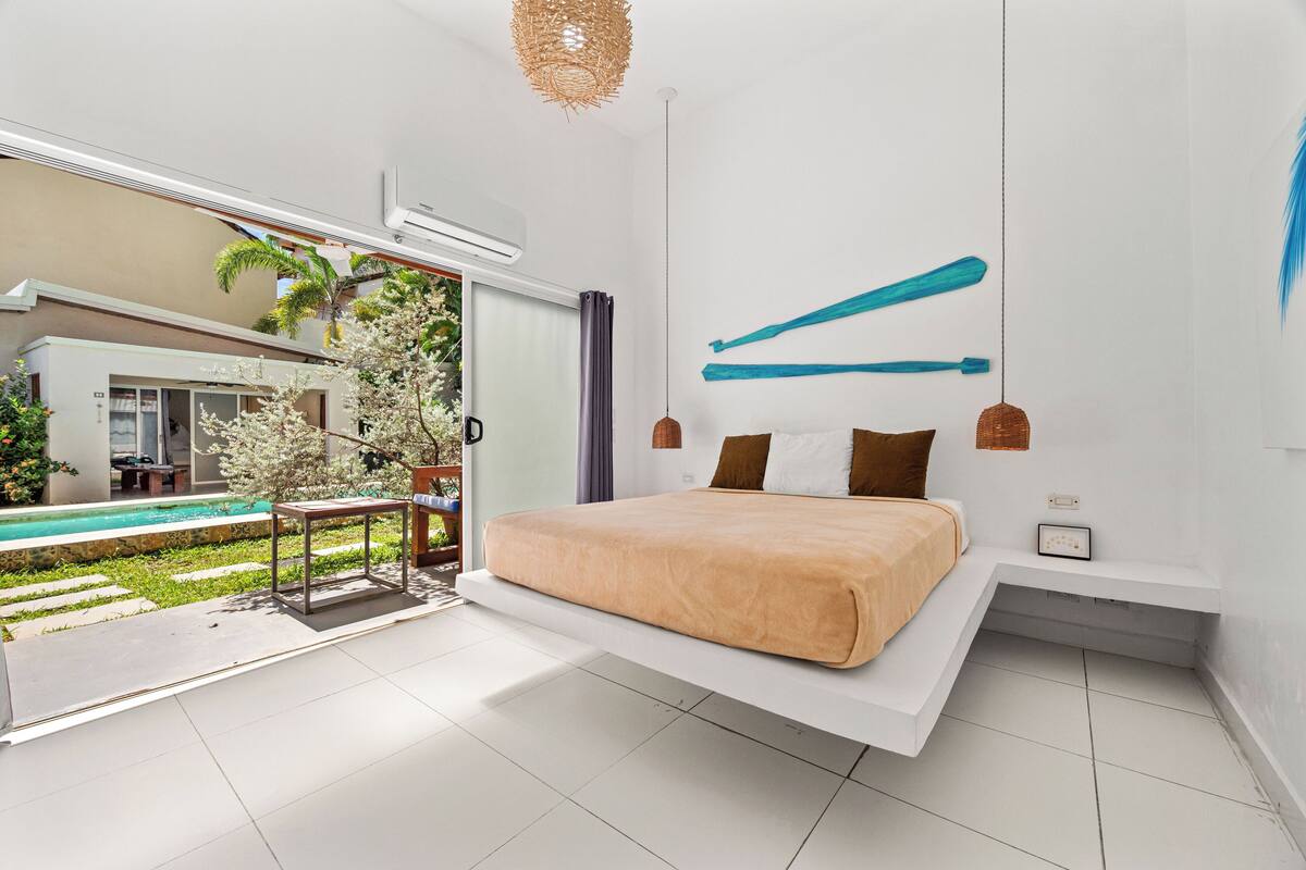 Een moderne slaapkamer met een bed, een hanglamp en uitzicht op een zwembad.