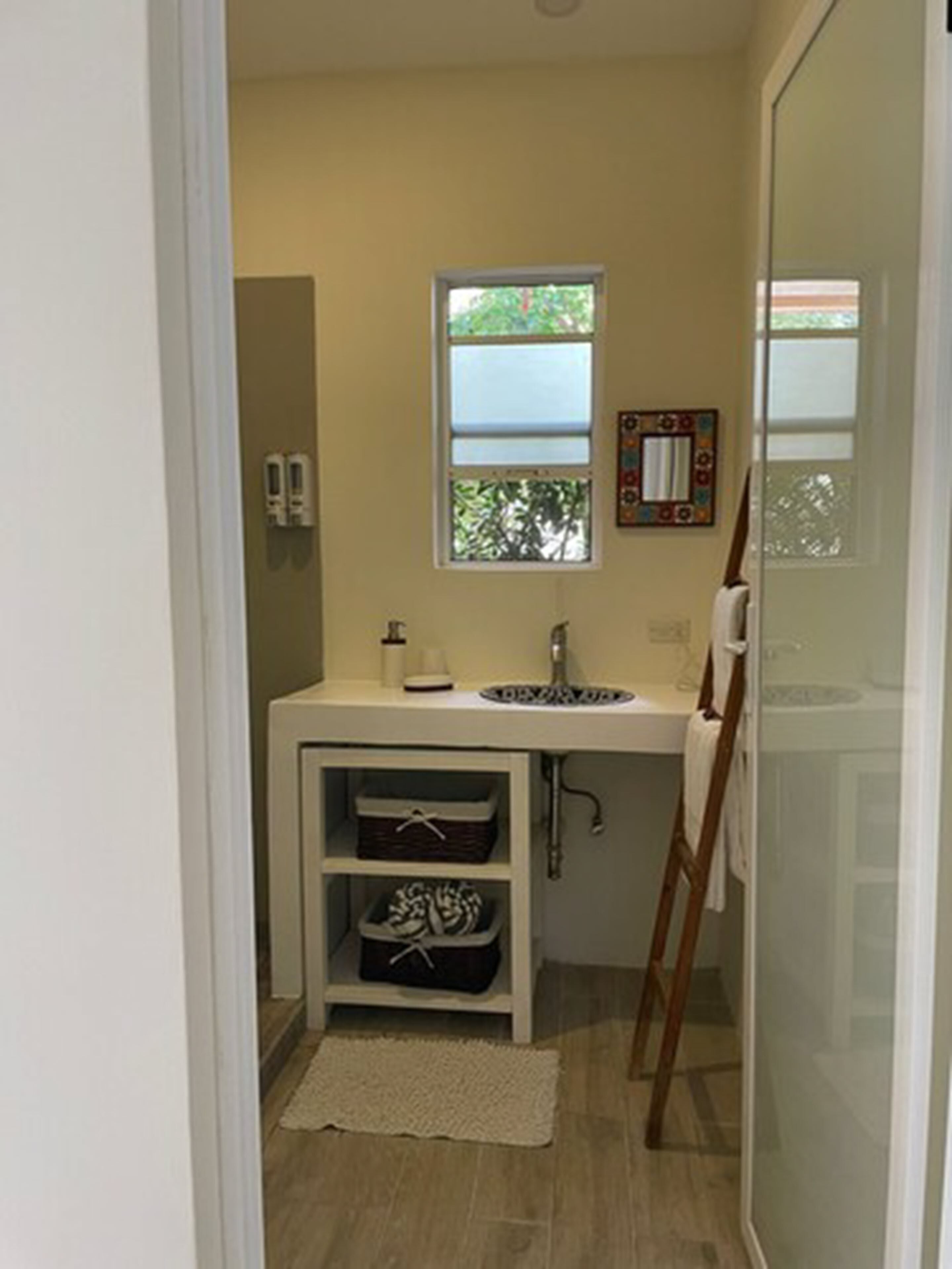 A bathroom with a white sink, a window above it, and a wooden ladder leaning against the wall.
