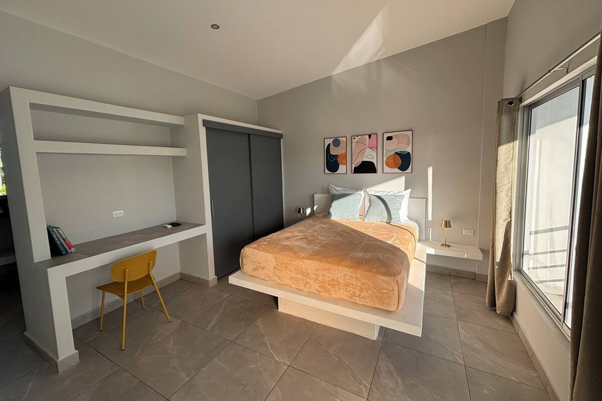 Een moderne slaapkamer met een bed, een bureau en een stoel. Boven het bed hangen drie decoratieve wandpanelen.