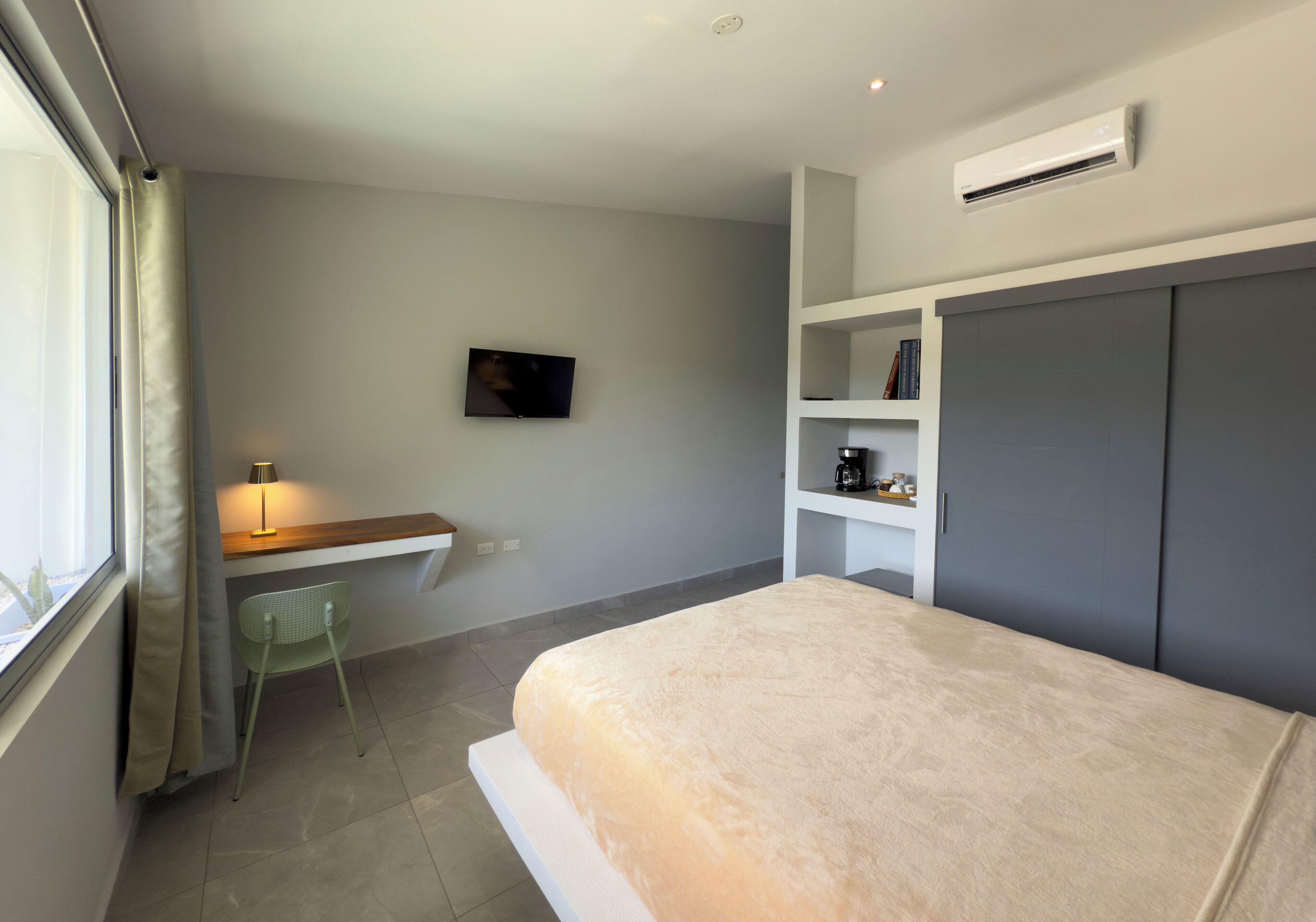 Un dormitorio con cama, escritorio con silla, televisor y almacenamiento empotrado.