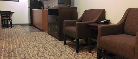 Un espace de vie compact comprenant un tapis à motifs, un coin cuisine, un téléviseur et deux fauteuils.