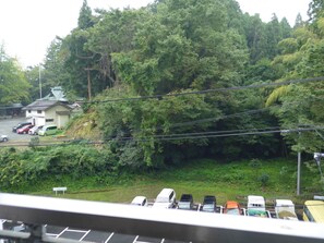 A parking area with several vehicles, a building with a sloped roof, and dense greenery in the background. - Koito Ryokan (Iwaki)