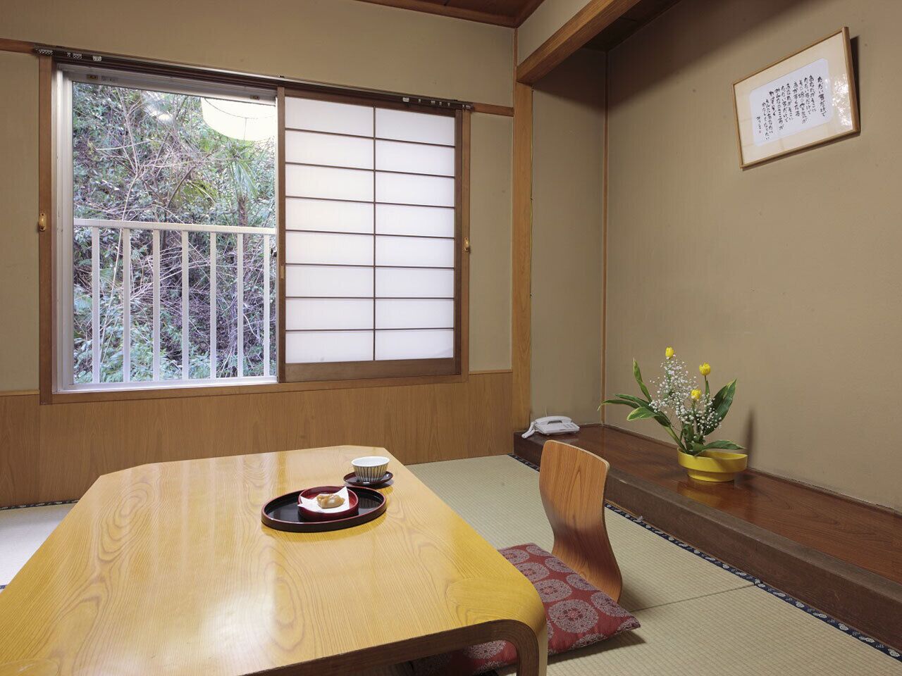 Una habitación japonesa tradicional con suelo de tatami, una mesa de madera con una bandeja de comida, un divisor de puertas shoji y una planta en maceta.