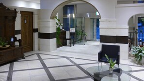 A lobby with a checkered floor, a wooden reception desk, a glass coffee table, and a seating area with a chair and a potted plant. - Koito Ryokan (Iwaki)