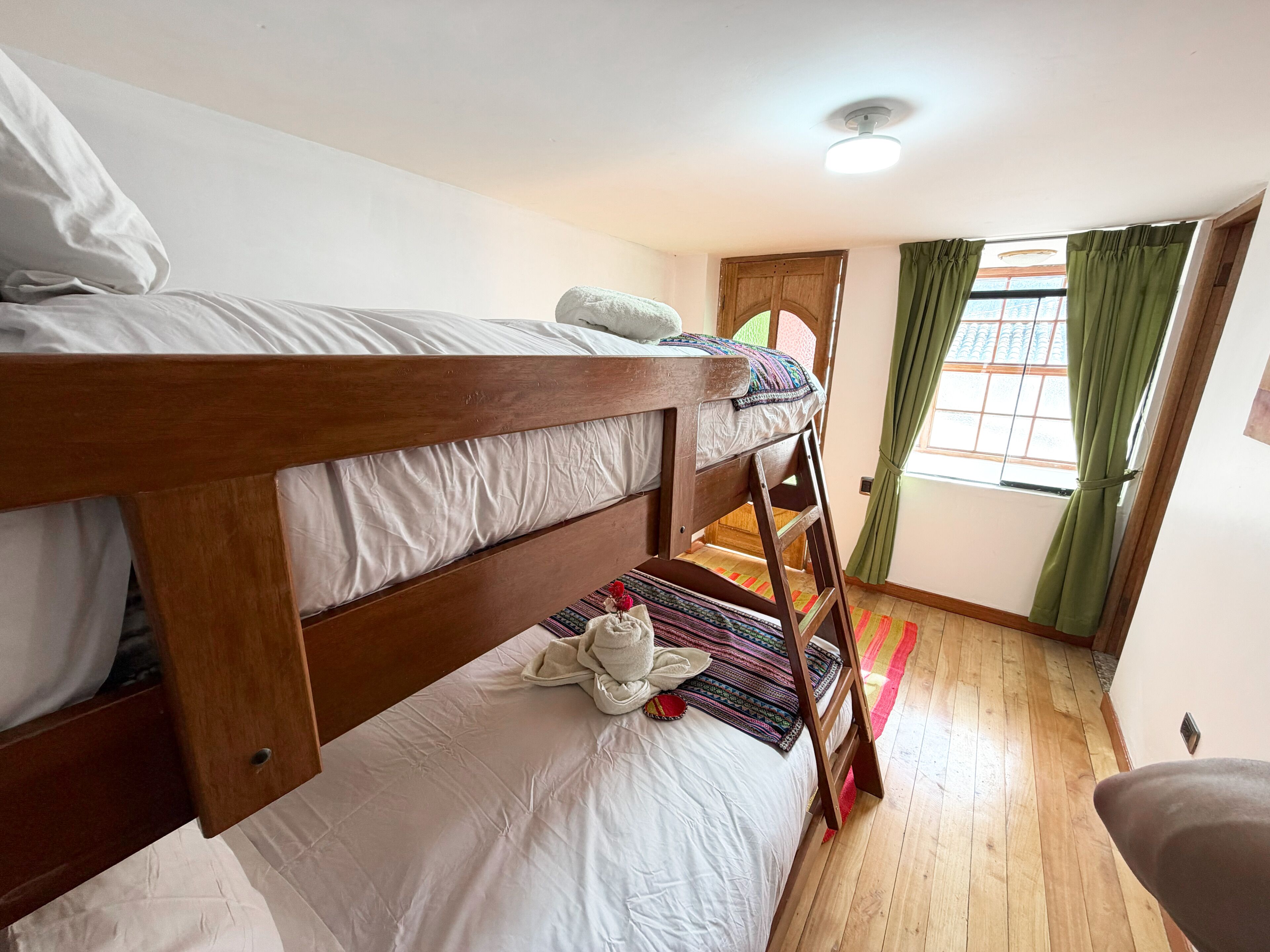 Una cama litera con ropa de cama blanca, una escalera de madera y una manta colorida.