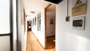 A hallway with wooden flooring, white walls, and a warning sign for electrical shock risk. - Hotel Inka King - Hostel (Ollantaytambo)