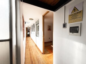A hallway with wooden flooring, white walls, and a warning sign for electrical shock risk. - Hotel Inka King - Hostel (Ollantaytambo)