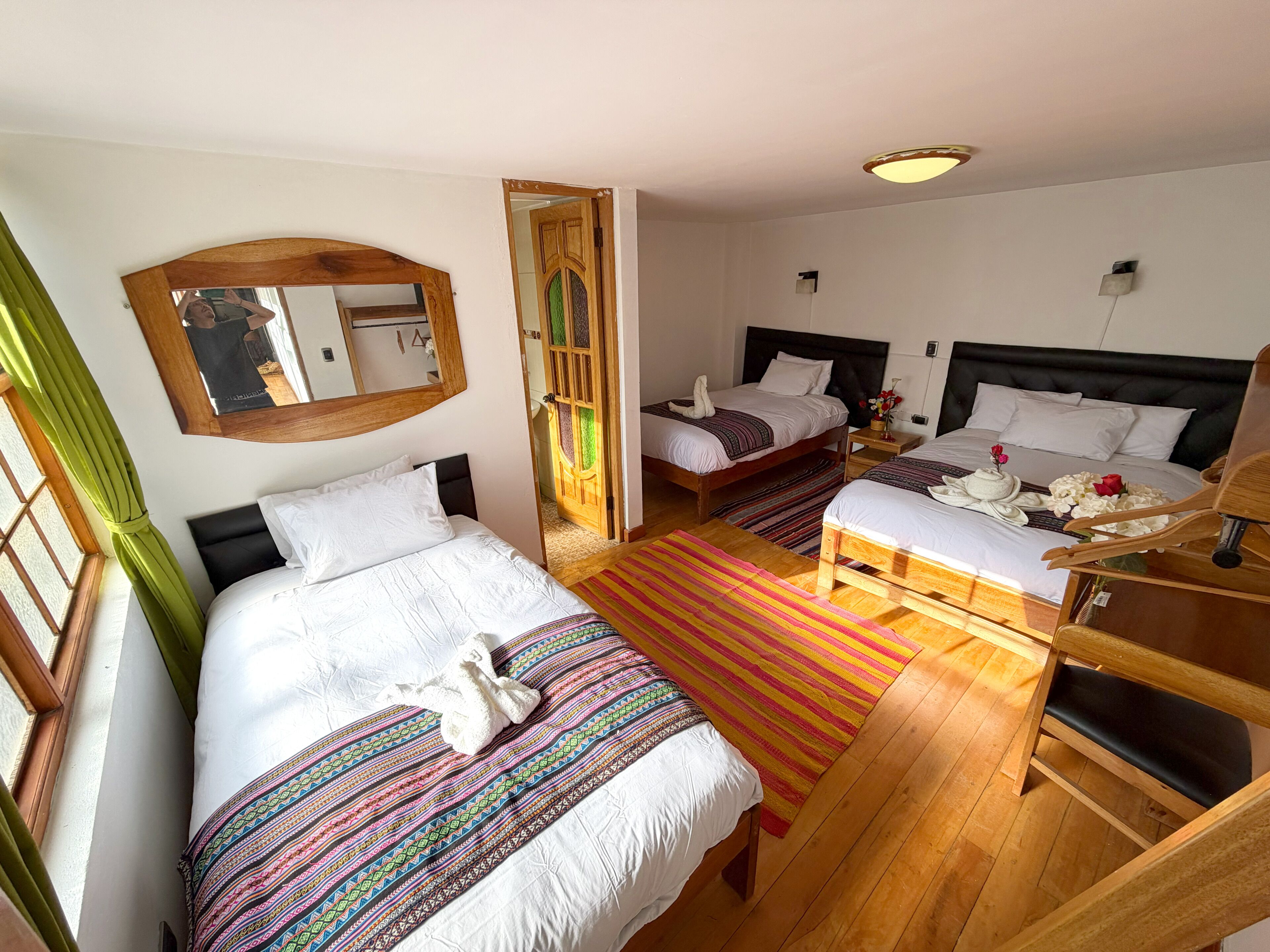 Una habitación de hotel con dos camas, un banco de madera, un espejo y una puerta que da a otra habitación.