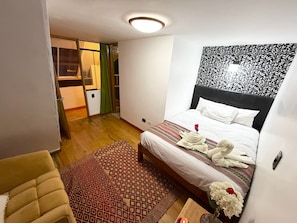 Ein Hotelzimmer mit Bett, kleinem Tisch mit Kerze, Stuhl, Teppich mit Muster und Wand mit Blattformen.