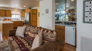 A cozy living room with a patterned sofa, wooden cabinets, and a kitchen area with a refrigerator and a glass display cabinet. - Inside Yosemite Lower Cascades (Yosemite National Park)