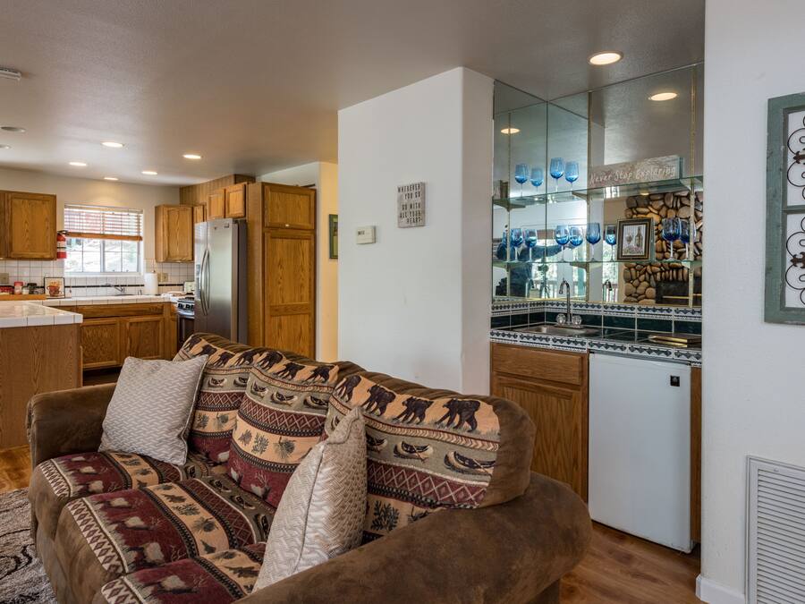 A cozy living room with a patterned sofa, wooden cabinets, and a kitchen area with a refrigerator and a glass display cabinet.